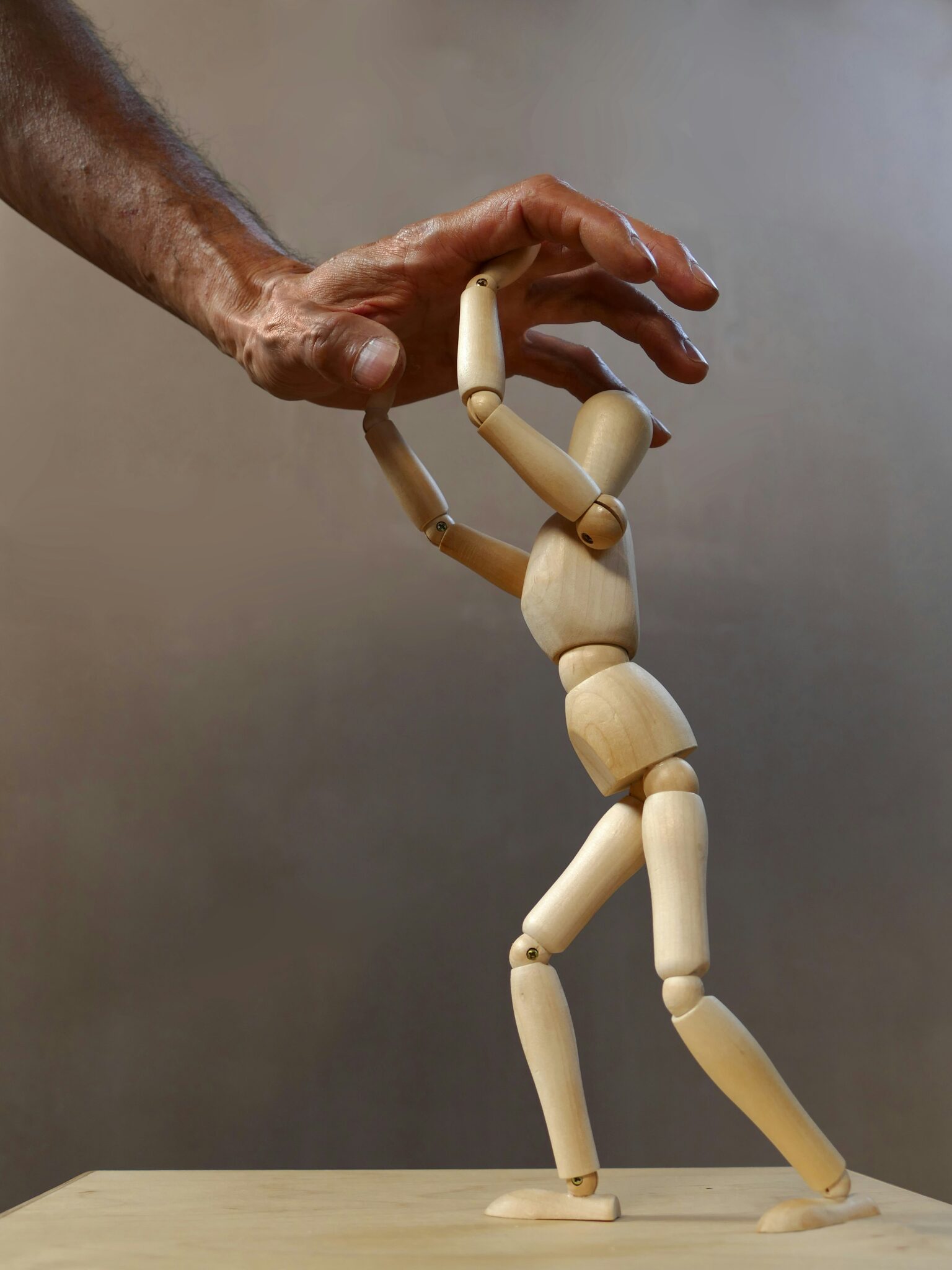 Figura de madera bajo una mano que presiona, representando el perfeccionismo y la autoexigencia