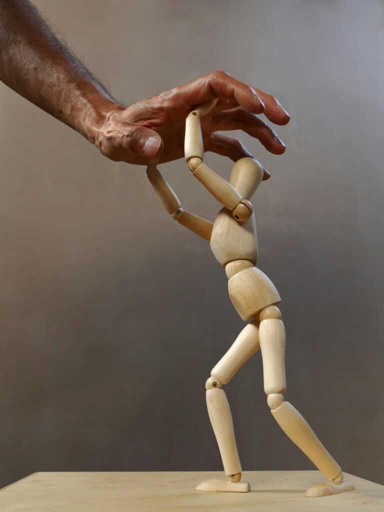 Figura de madera bajo una mano que presiona, representando el perfeccionismo y la autoexigencia